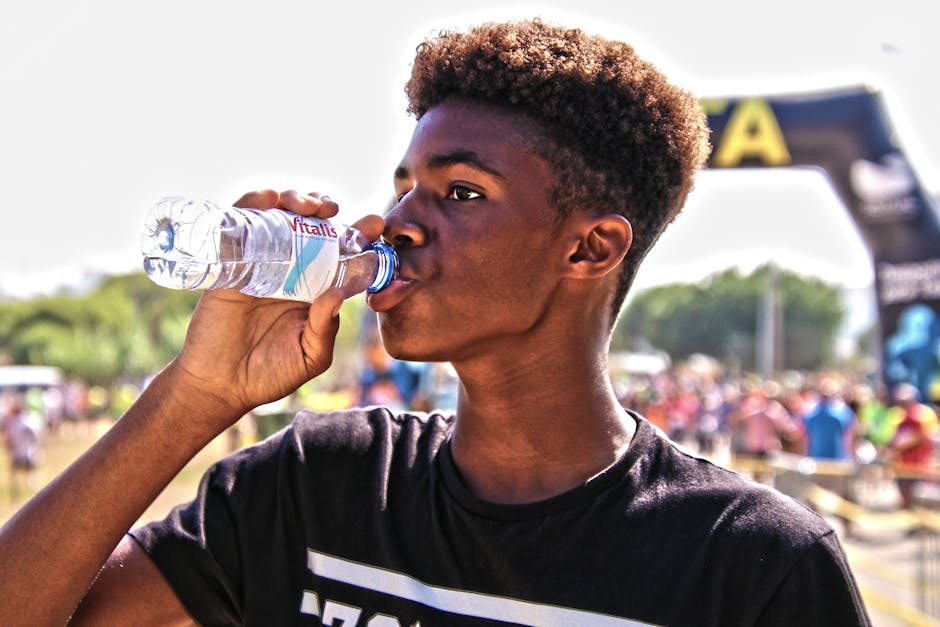 A young man drinking bottled water outdoors at a sporting event, showcasing hydration and fitness.