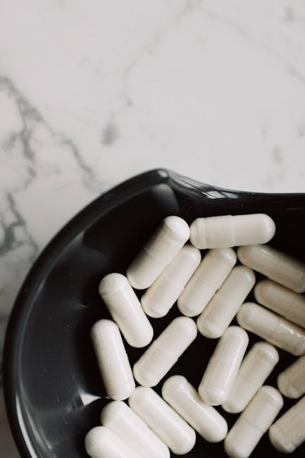 A close-up view of white capsules in a black bowl on a marble surface, emphasizing medicine and health.