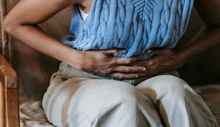 Young African American female sitting on couch at home while having acute pain in stomach
